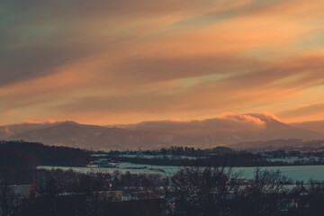 colorful sunset clouds over the countryside in czech republic with snow and mountains in the background on a winter day