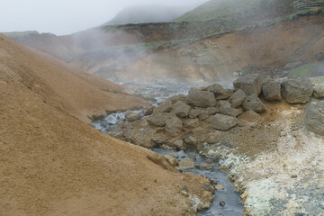 volcanic landscape with sulphur gases evaporating and a river with rocks