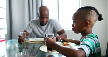 Candid black African family eating lunch, dad putting away phone, child drinking soda beverage