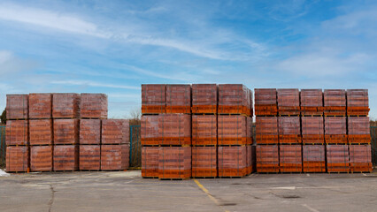Red brick packed in stacks are stored on ground outdoors at a hardware store warehouse. Building bricks on pallets on an outdoor warehouse.