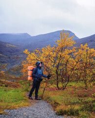 Obraz premium A woman with a backpack in the autumn season walks along a path in the mountains on a rainy day.