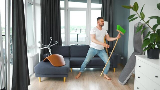 Man cleaning the house and having fun dancing with a broom. Slow motion