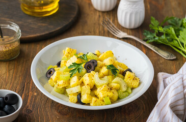 Potato salad with green selery and olives in a gray ceramic bowl on a wooden background. Recipes for potato salads. Healthy food.