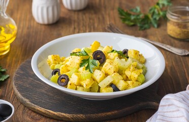 Potato salad with green selery and olives in a gray ceramic bowl on a wooden background. Recipes for potato salads. Healthy food.