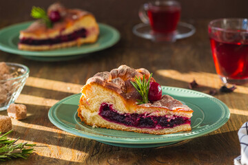 Sliced round yeast dough pie with cherries on a green ceramic plate on a brown wooden background.