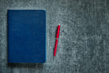 Blue leather business diary and red ballpoint pen on gray office table