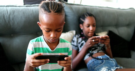 African siblings using cellphone at home. Black ethnicity children watching video on cellphone