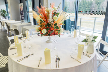 Big floral wedding centrepiece, made out of white roses and pampas grass on a white table in a reception venue.