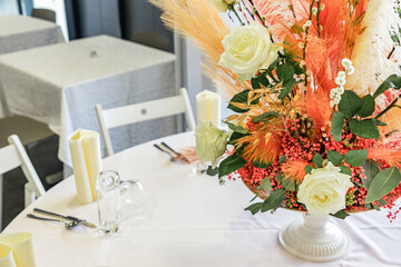 Big floral wedding centrepiece, made out of white roses and pampas grass on a white table in a...
