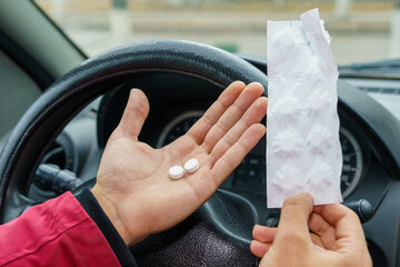 Two pills in the hand or on the palm of the driver against a blurred background of the steering...