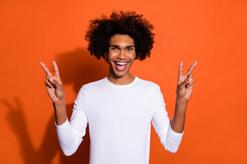 Photo of excited sweet guy dressed white shirt smiling showing two v-signs isolated orange color background