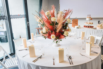 Big floral wedding centrepiece, made out of white roses and pampas grass on a white table in a reception venue.
