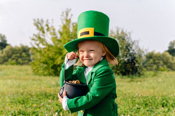 Portrait of a beautiful little girl in a leprechaun costume who holds a pot of gold coins in her...
