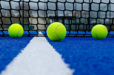 Selective focus. Net of a blue paddle tennis court and three balls near the white line