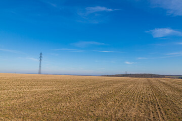 Obraz premium High voltage poles for electricity distribution in the countryside. In the background is a blue sky with dramatic clouds.
