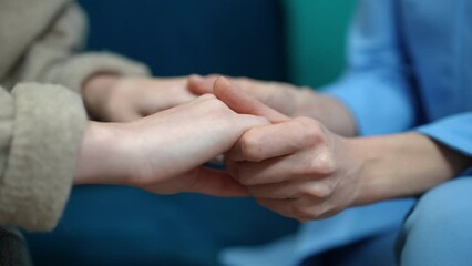 Close-up Caucasian women holding hands sitting on sofa indoors. Unrecognizable psychologist therapist and teenage girl palms. Support and endorsement concept