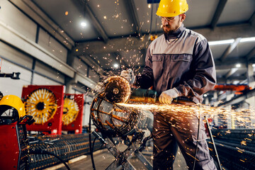 A metal and iron factory worker processing metal construction with grinder. - Powered by Adobe