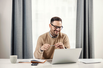 A happy freelancer sitting at his home office, working and looking at the laptop.