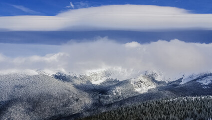 Obraz na płótnie Canvas Beautiful panoramic view of Colorado mountain range with ski bowl covered with clouds; blue sky and large cloud formation in background
