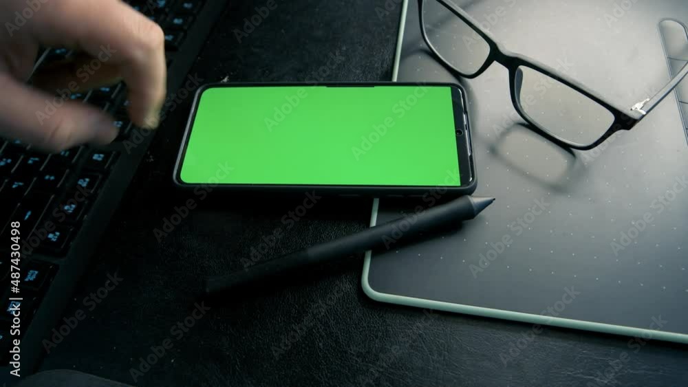 Poster man using mobile phone at his working place with the light on monitor. 4k video footage with green s