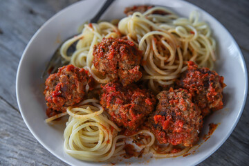 Meatballs in tomato sauce with spaghetti on a gray wooden background, close up. Italian homemade food 