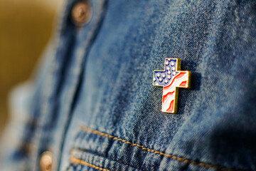 Close up of Christian cross pin with American flag colors is pinned on blue jeans jacket....
