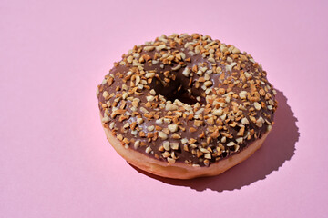 Donut covered with icing, with nuts, top view on trendy pink  background. Flat lay style.