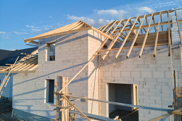 Aerial view of unfinished frame of private house with aerated lightweight concrete walls and wooden roof frame under construction