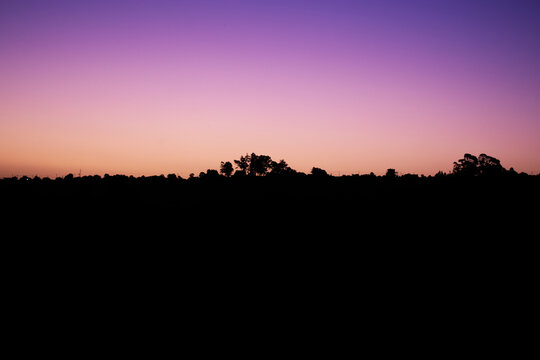 landscape in silhouette between the mountains and the sky painted in violet and pink colors in gradient at sunset time