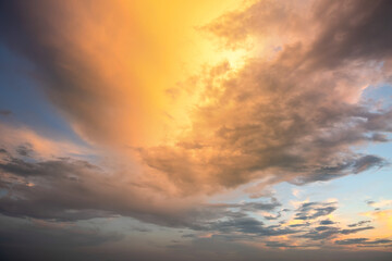 Dramatic sunset sky landscape with puffy clouds lit by orange setting sun and blue heavens.