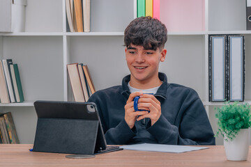 teen boy at home with cup looking at computer or screen © carballo