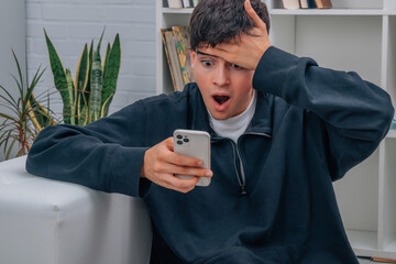 teen boy at home astonished looking at mobile phone © carballo