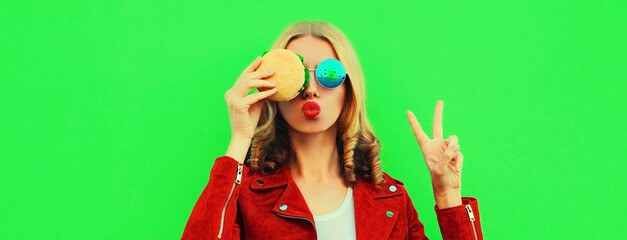 Obraz na płótnie Canvas Portrait of stylish young woman eating tasty big burger fast food on green colorful background