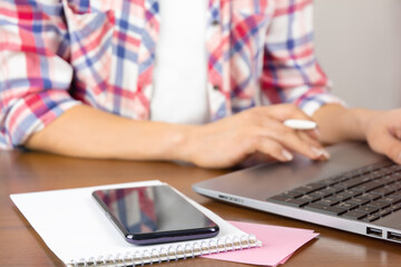 Home workplace. Woman using laptop on table with notes and smartphone. Working at home concept