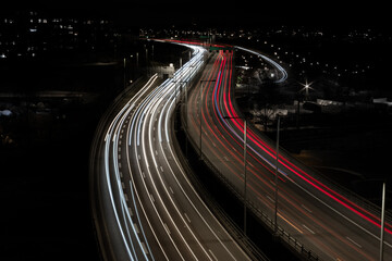 Cars and trucks driving at night over a bridge on a higly trafficated road in the middle of a city over a river