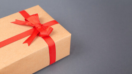 Close up gift box, wrapped in kraft paper with a red bow on a dark gray background. Copy space.
