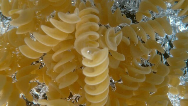 Super slow motion of falling uncooked italian pasta Fusilli into water, black background. Filmed on high speed cinema camera, 1000 fps.