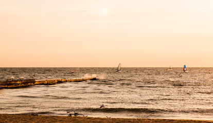 Silhouettes of windsurfers in the sea at the sunrise. People are doing sports at the dawn. Orange colours of the sunrise makes the sae look majestic.