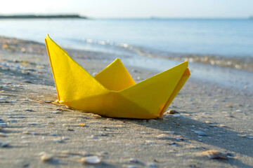 SSmall paper yellow boat on sand near water on background of sea waves closeup. Paper boat on sandy...