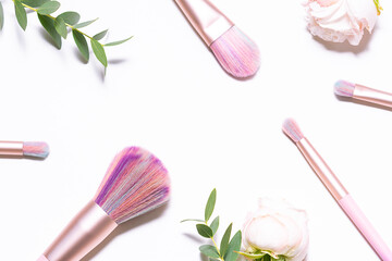 Bright colorful make up brushes with rose flowers and eucalyptus twigs on white background with...