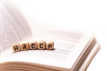 the word HACCP spelled on an open book with wooden letters, concept picture with white background