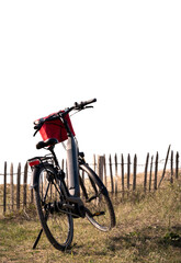 Black Electric bike with a red basket parked in grass against fence on white background for copy...