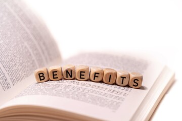 the word BENEFITS spelled on an open book with wooden letters, concept picture with white background