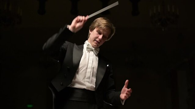 The camera moves away from the conductor of the string orchestra. Slow motion