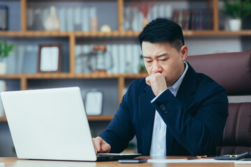 Sick asian businessman working on laptop in office, man coughing