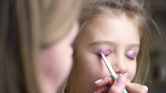 mother uses a brush to apply shiny shadows on eyelids of her daughter