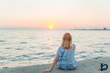 Fototapeta na wymiar Young blond woman sitting near the sea at sunset