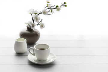 The atmosphere of a romantic morning, morning coffee. Flowering branches in a vase and a cup of coffee on a white wooden background. Lifestyle.Copy space.