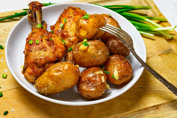 tasty lunch in rural style, healthy food - fried chicken meat and unpeeled roasted potatoes on a dish, green leek, salt and garlic, cooked food on a white wooden boards