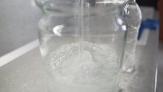 Moonshine pours into a large jar. Home production of alcohol. A close-up of alcohol is poured into a special flask.